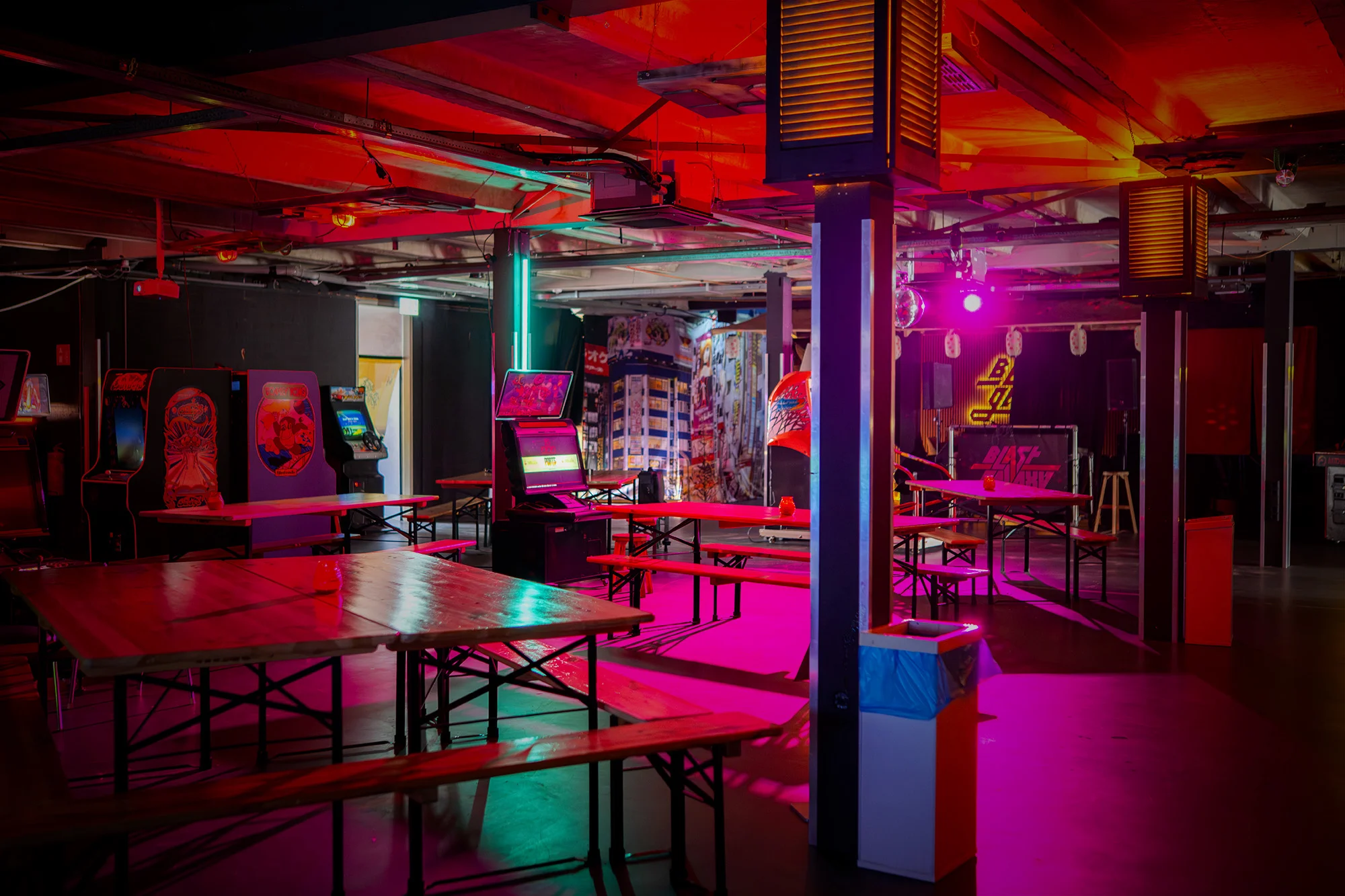Tables and benches beside the arcade games under red and pink lighting at Blast Galaxy